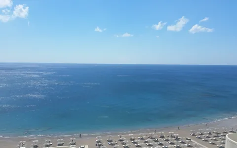 Beach umbrellas beside the blue sea on the coast of Rhodes, Greece.