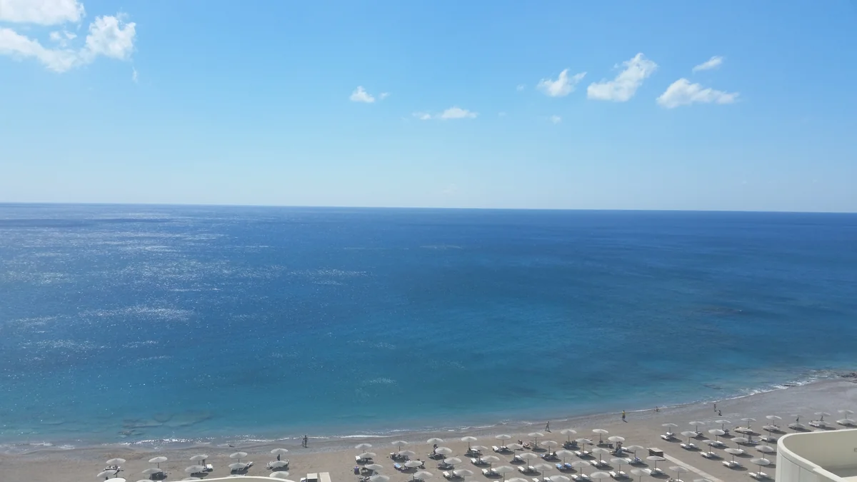 Beach umbrellas beside the blue sea on the coast of Rhodes, Greece.
