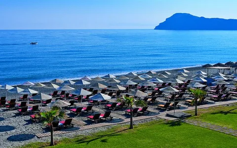 Beach umbrellas and a green lawn at Minoa Palace Resort, with an island across the sea.