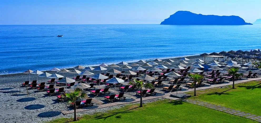 Beach umbrellas and a green lawn at Minoa Palace Resort, with an island across the sea.