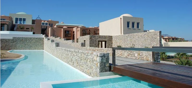Pale stone resort buildings and a bridge beside a pool at Helona Resort, Kos.