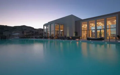 Illuminated glass-fronted building beside a swimming pool at dusk at Helona Resort, Kos.