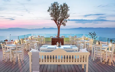 White tables and chairs on a restaurant terrace overlooking the sea in Rhodes at sunset.
